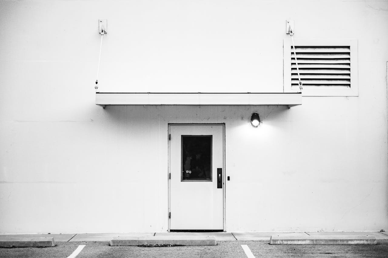 Black and white photo showcasing a minimalist white exterior with a centered single door and small awning.